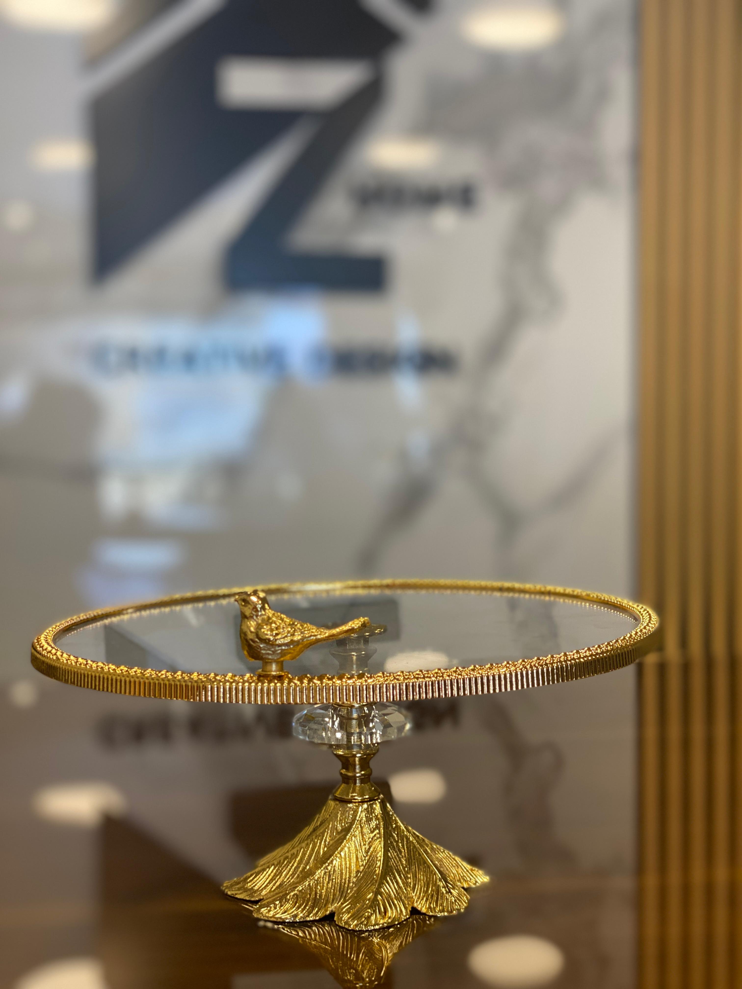 A decorative glass cake stand with a golden base and a bird ornament